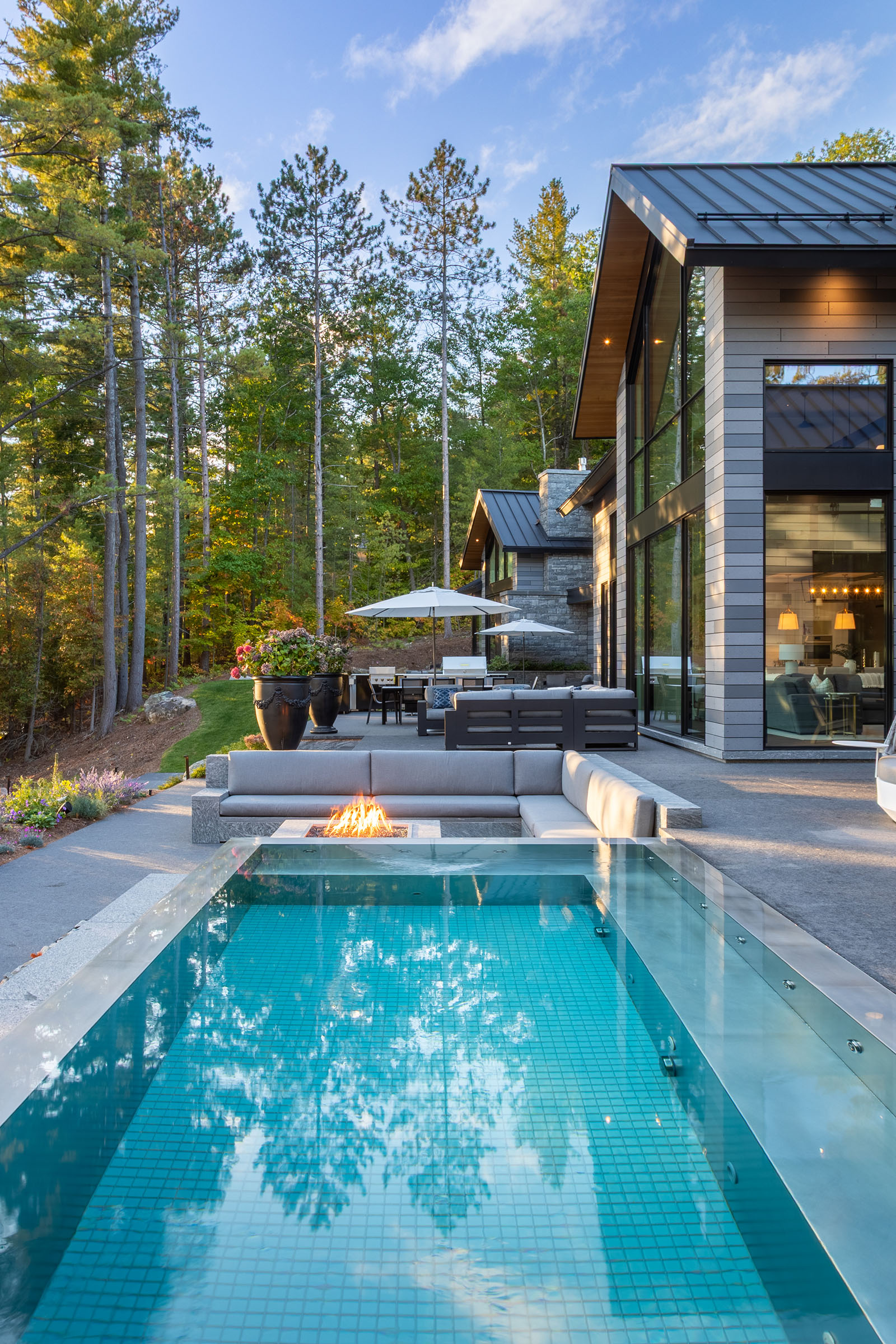 Modern backyard with swimming pool, two lounge chairs under a large white umbrella, and a gray sofa with cushions.