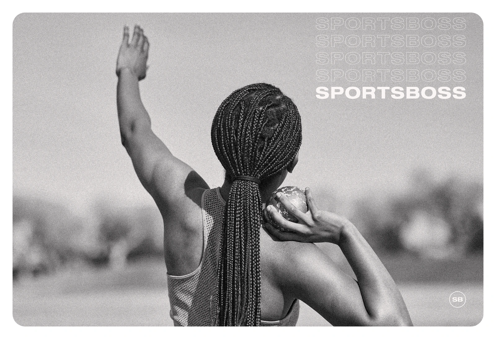 A track and field athlete photographed from behind, one arm raised, holding a shot put at her shoulder before a throw.