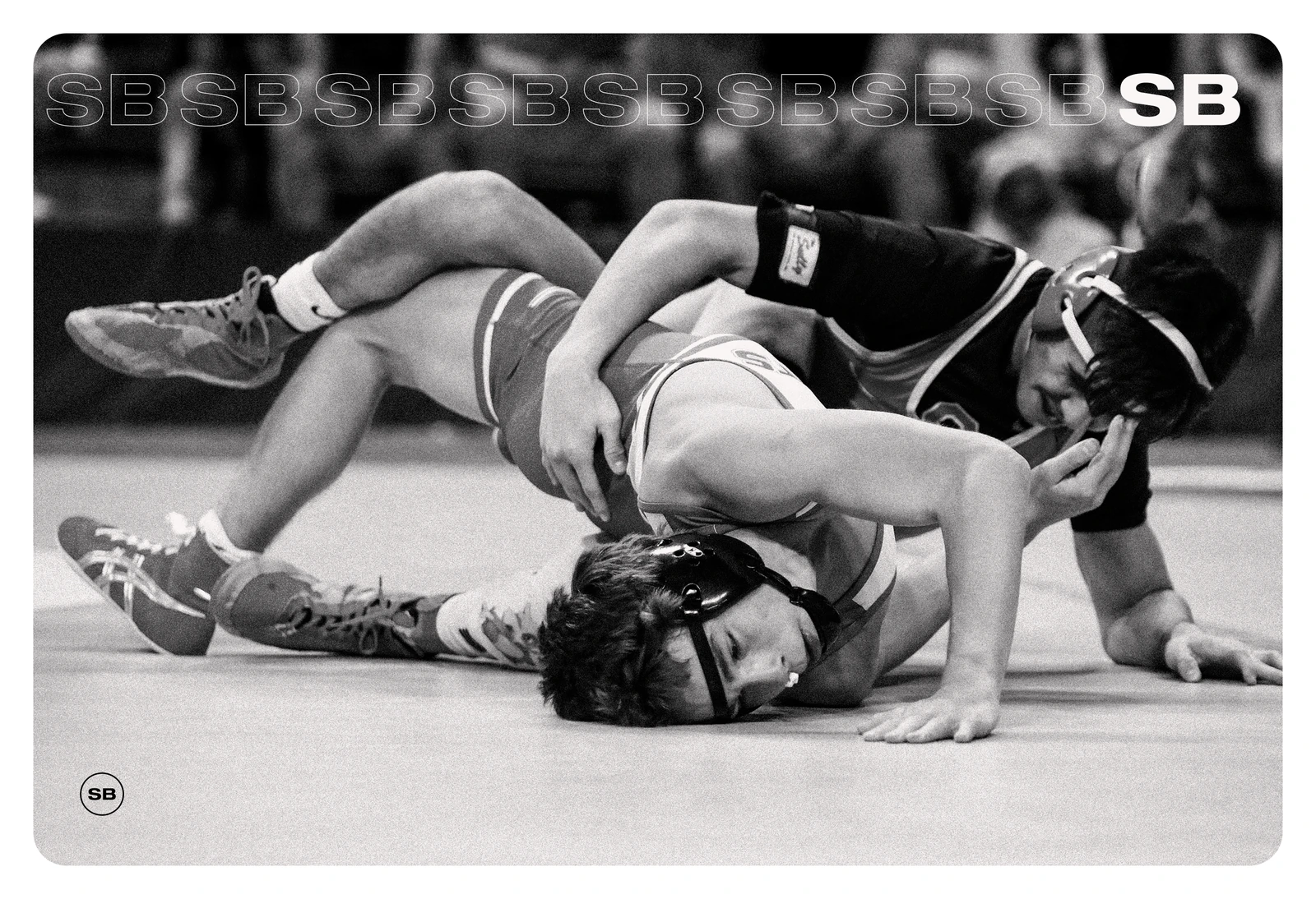 Two high school wrestlers on the mat, one working to turn his opponent onto his back during a match.