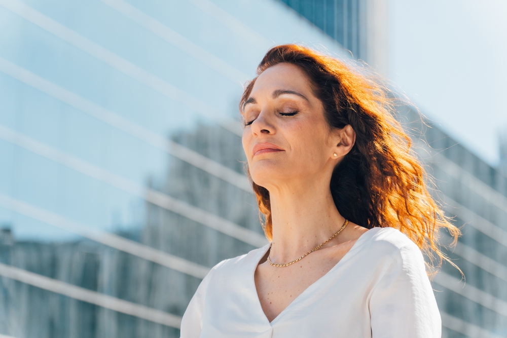 Female presenting professional outdoors with eyes closed clearly taking a breath