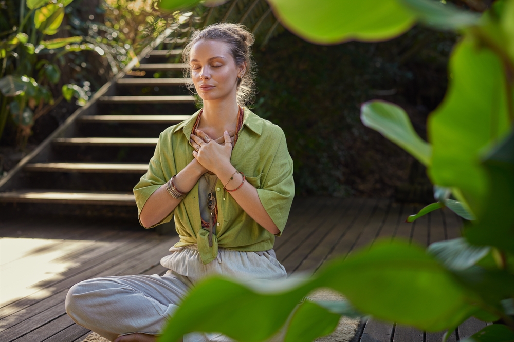 Woman dressed in comfortable clothing meditating in a sunlit area by a staircase