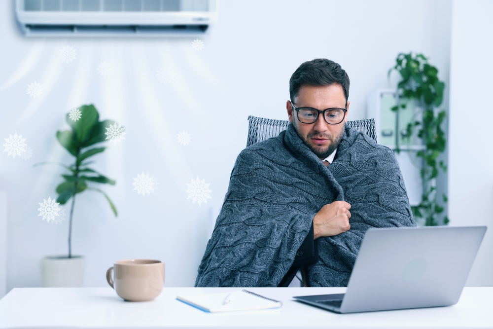 Male presenting human in office wrapped in a knit blanket