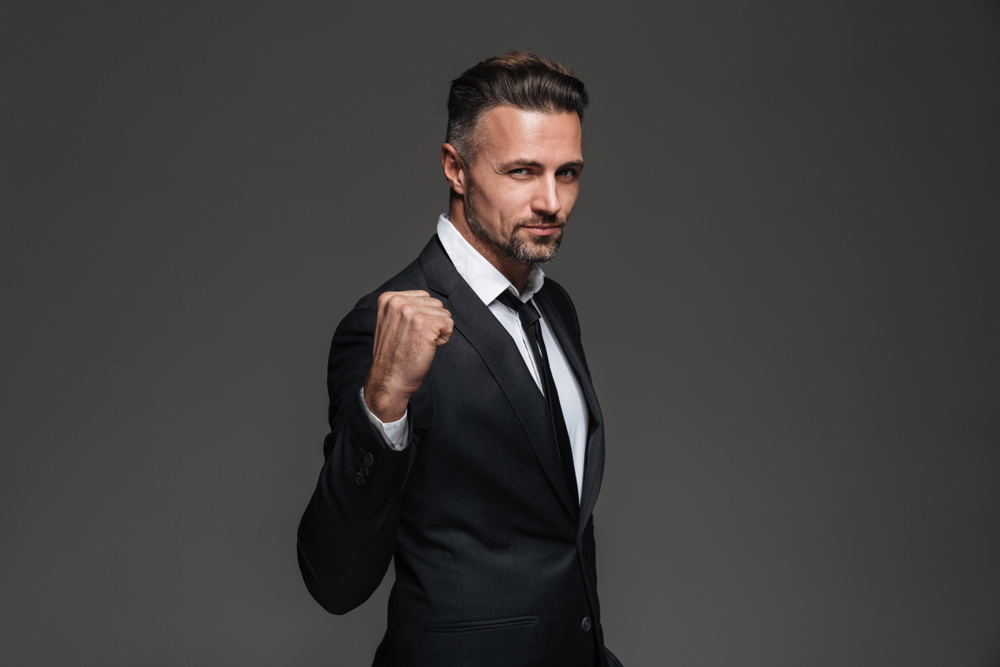 White presenting, male presenting person in a dark suit in profile with a raised fist. Performing confidence.