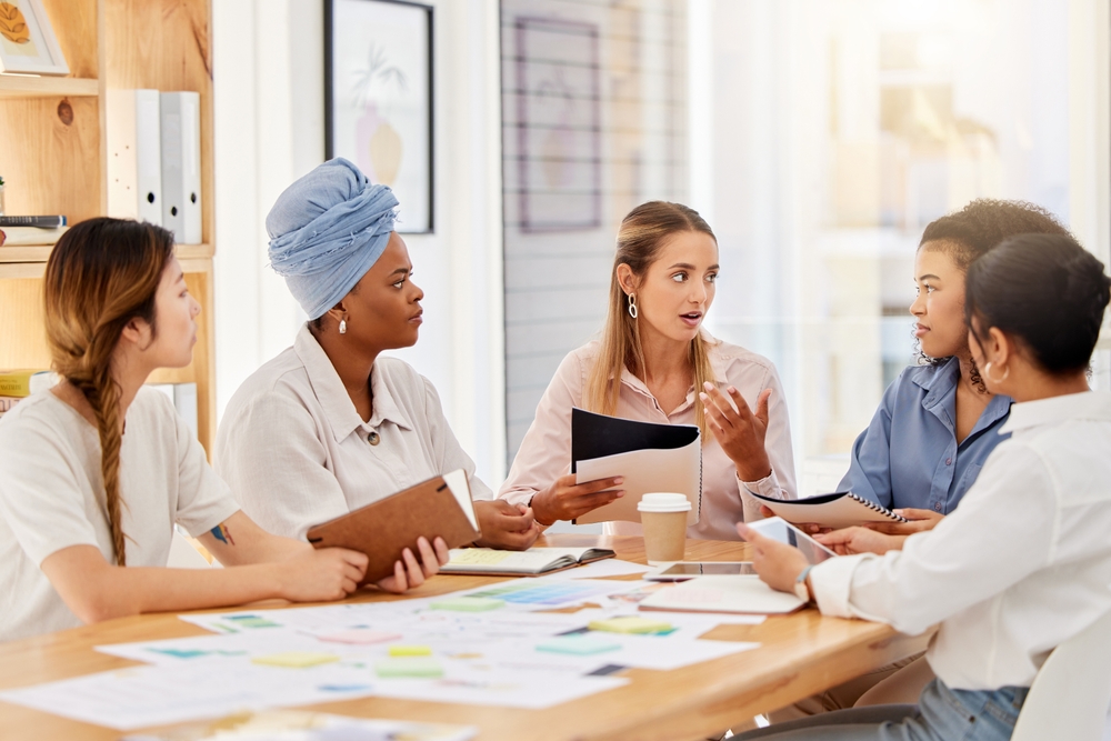 Small meeting (5 diverse people) engaged with a young woman leading.
