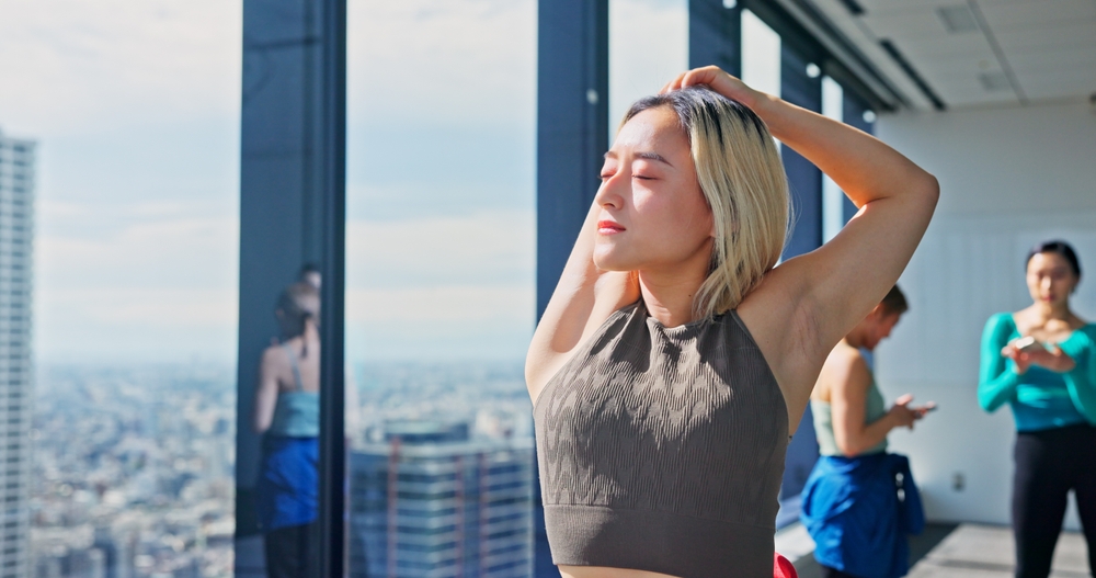 Blonde, female presenting person of Asian decent stretching with other dancers in the background