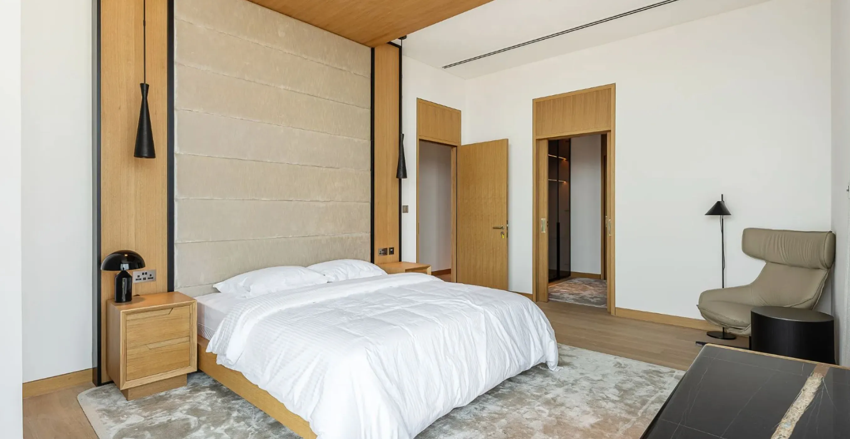 Minimalist bedroom interior fit-out in Palm Jumeirah featuring white bedding and wood panels.