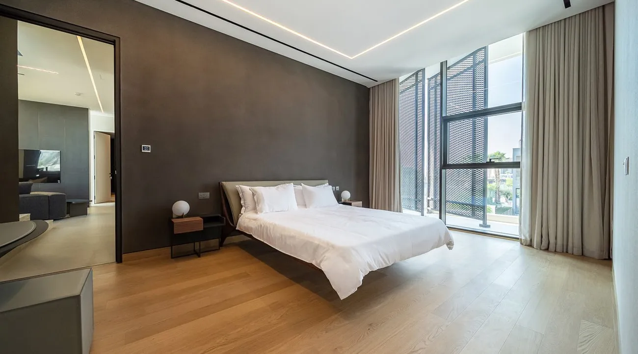 Modern bedroom interior design with white bedding and recessed ceiling lighting in Dubai Hills.