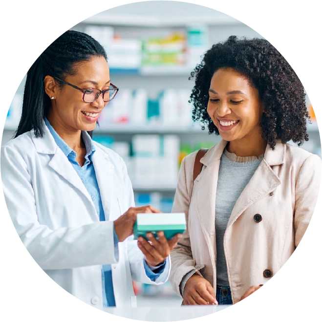 Pharmacist smiling and showing a medication box to a female customer in a pharmacy.