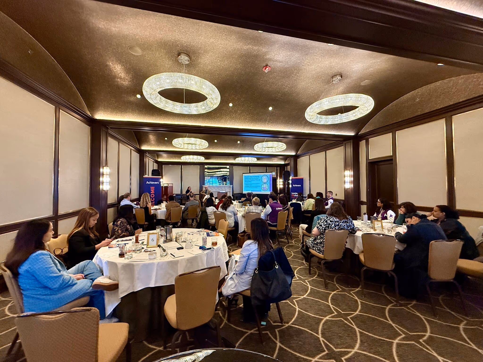 Business conference with attendees seated at round tables under crystal chandeliers