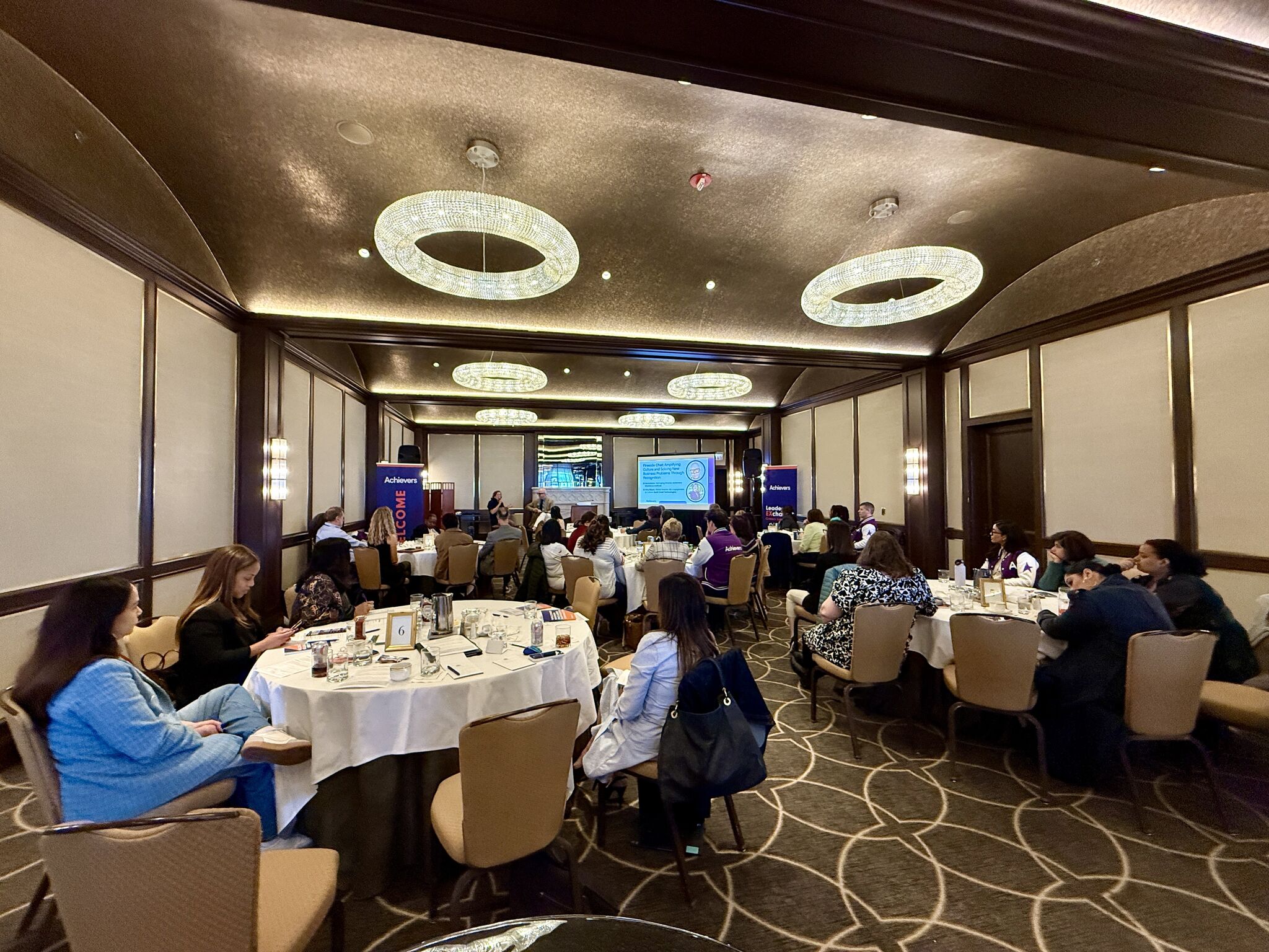 Business conference with attendees seated at round tables under crystal chandeliers