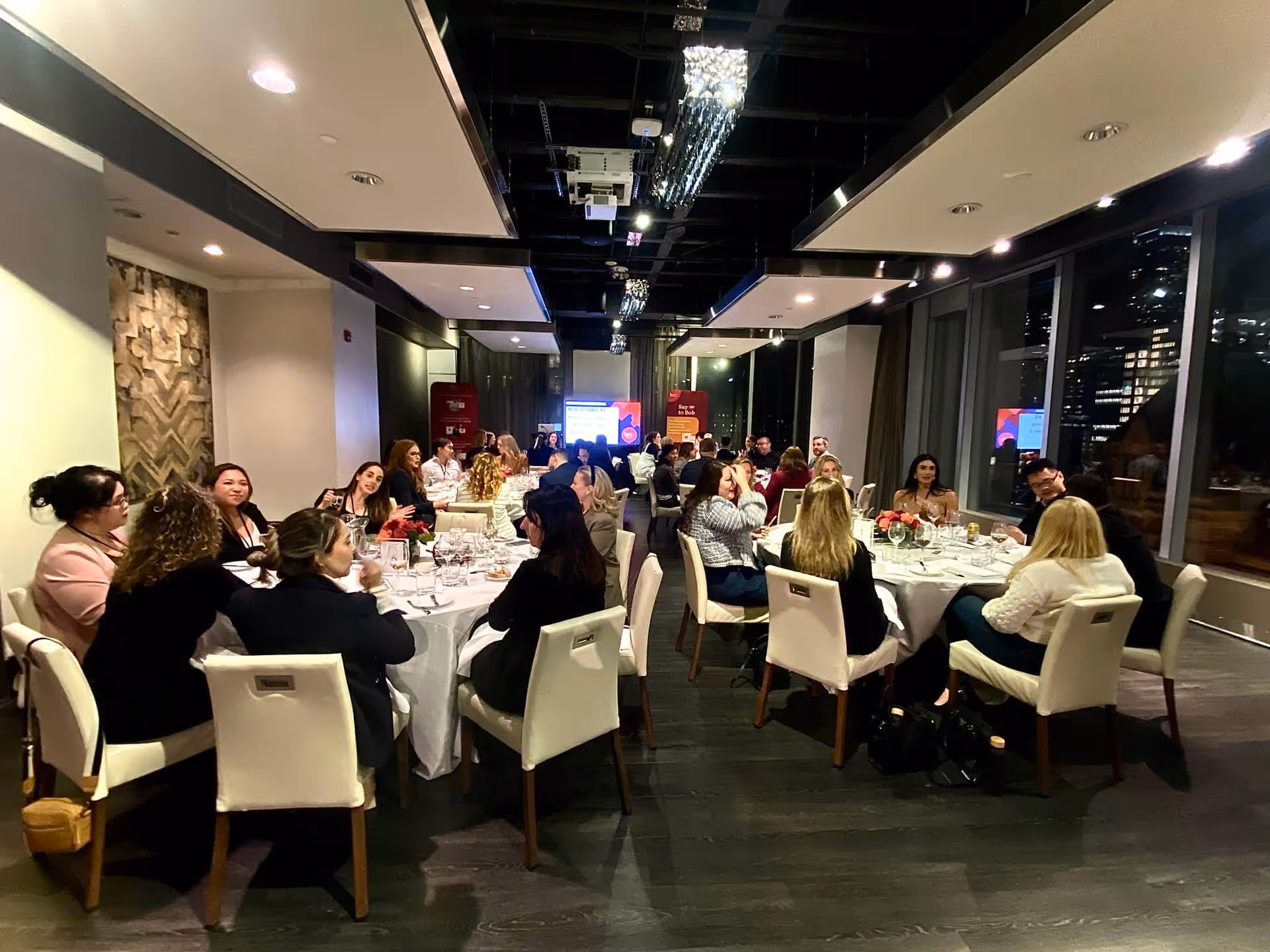 Evening professional networking dinner with groups seated at white-covered tables
