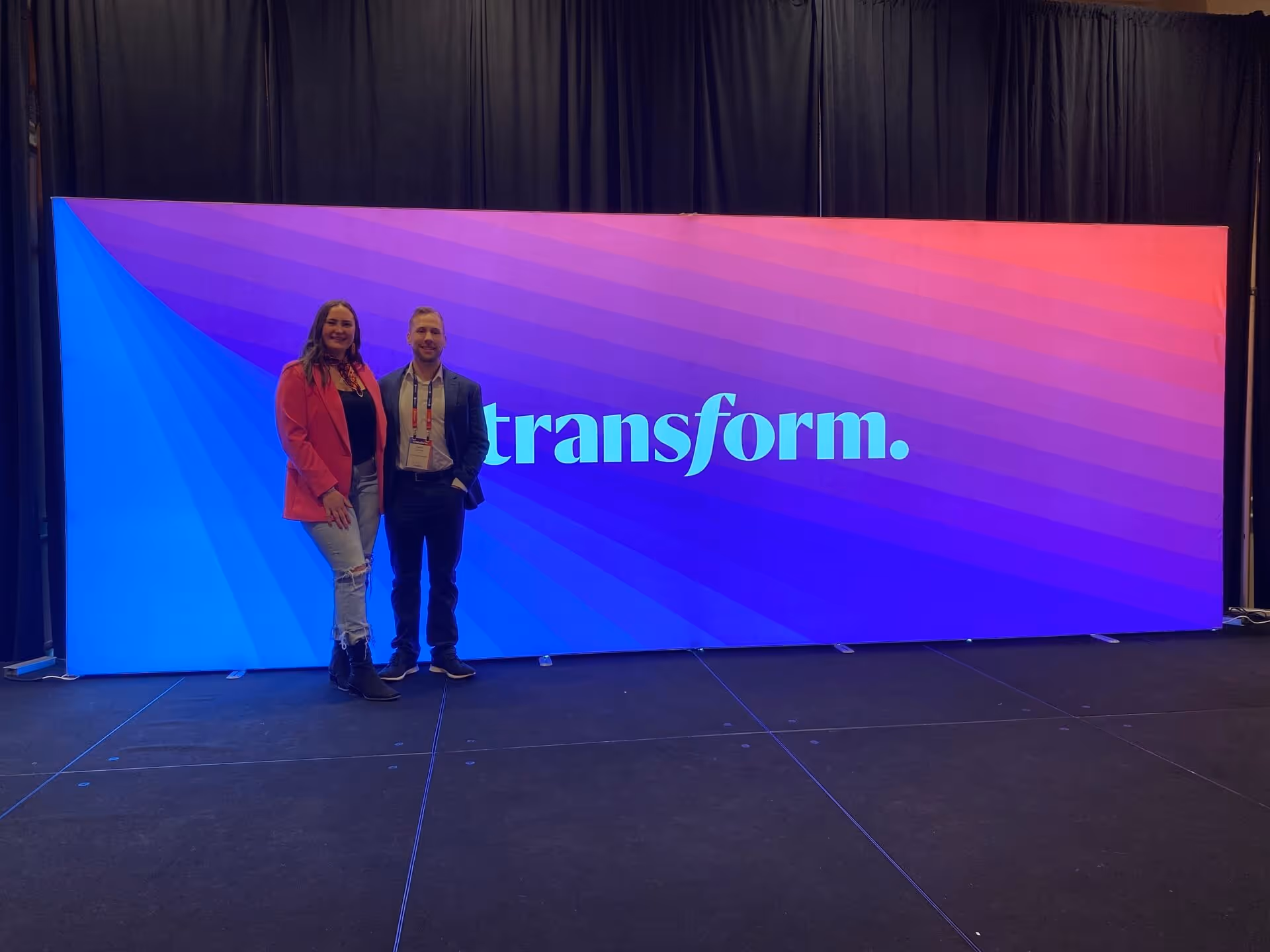 Two people standing in front of colorful Transform conference backdrop