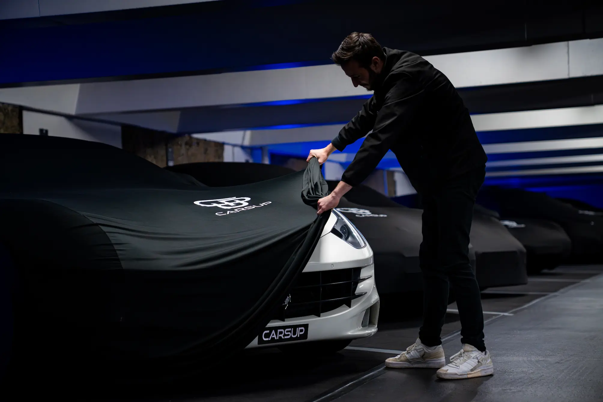 Expert Carsup retirant délicatement une housse de protection personnalisée sur une Ferrari blanche dans un parking sécurisé Carsup