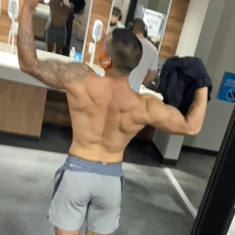 Muscular man flexing back and arm muscles in gym locker room in front of mirror.