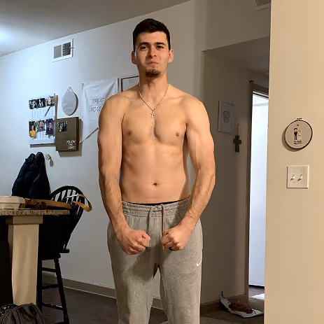 Young man shirtless in gray sweatpants standing with fists clenched indoors.