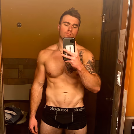 Muscular man with tattoo takes shirtless mirror selfie wearing black Reebok underwear.