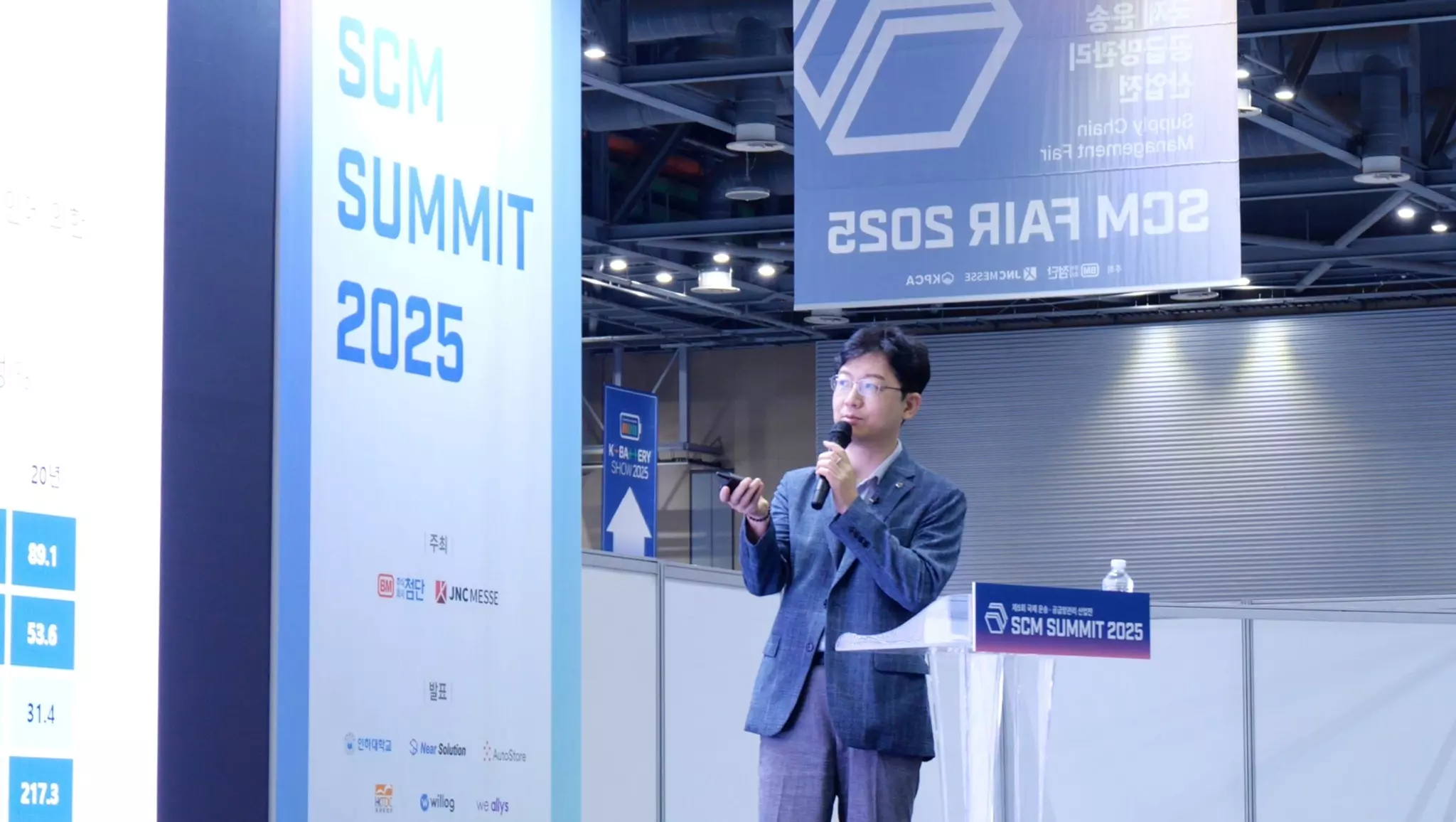SCM 서밋 2025 행사장에서 발표자가 마이크를 들고 발표하는 모습, SCM과 ERP 통합 관리 관련 최신 동향과 기술을 공유하는 비즈니스 컨퍼런스 현장