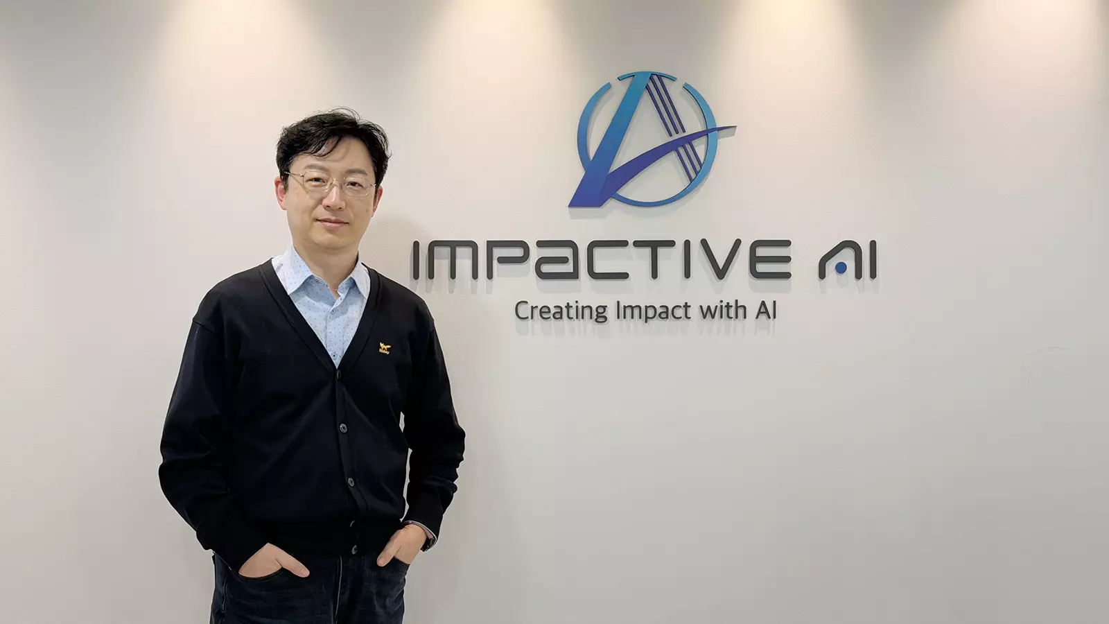 임팩티브AI 회사 로고와 슬로건 ‘Creating Impact with AI’가 새겨진 벽 앞에서 포즈를 취한 남성 기업 임직원의 모습, 첨단 기술 솔루션 전문 기업의 이미지