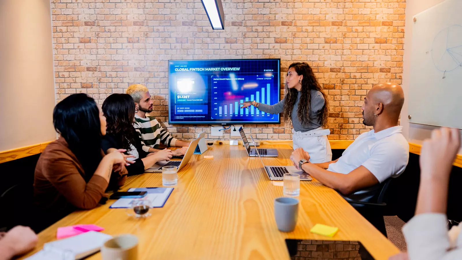 A professional team collaborating in a meeting room using a demand forecasting solution to analyze market data on a large screen for collective decision-making