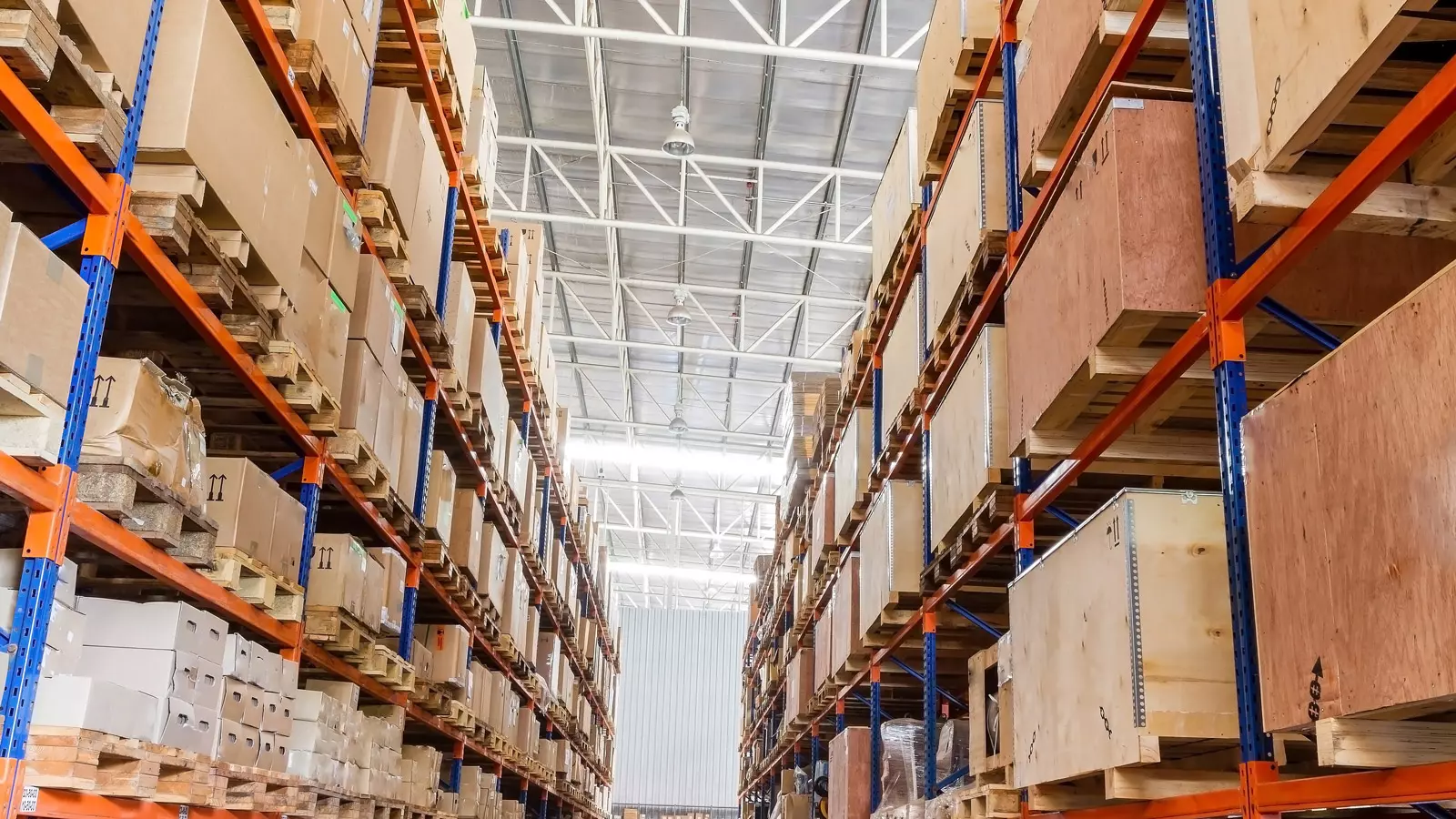 대형 물류 창고 내부에서 직원이 높은 선반에 가득 찬 재고 물량을 확인하며 관리하는 모습