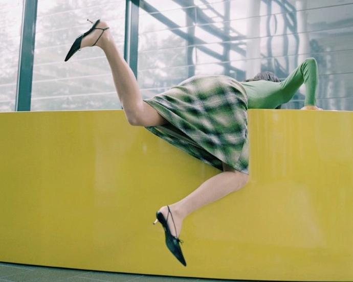 A person in a dress and heels falling from a yellow wallDescription automatically generated
