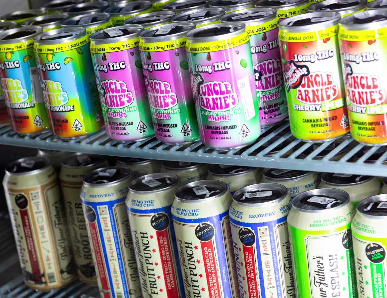 Refrigerated display filled with colorful cannabis-infused beverage cans, including Uncle Arnie’s lemonade and watermelon drinks on the top shelf and Alpine Splash and fruit punch varieties below, all labeled with THC content.