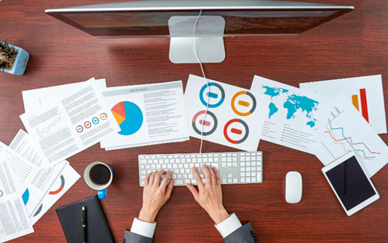Business analytics workspace with multiple dashboards, charts, and reports spread across a desk, illustrating fragmented KPIs and reporting complexity for marketing teams. i-radius