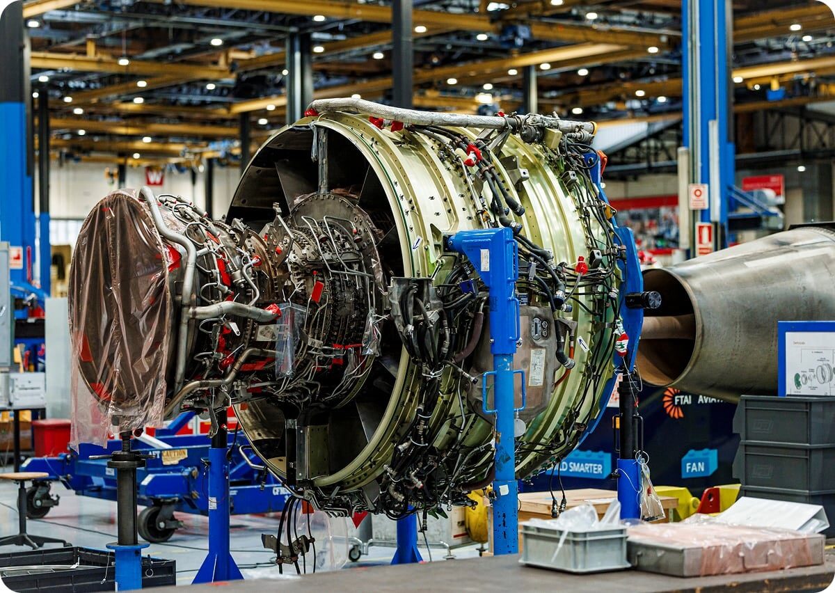 Motor de avión en proceso de mantenimiento o ensamblaje en un taller industrial con soporte azul y tubos metálicos visibles.
