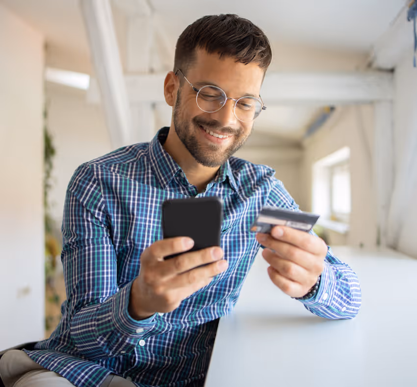 Person holding credit card in front of a laptop with digital security shield and technology icons overlay.