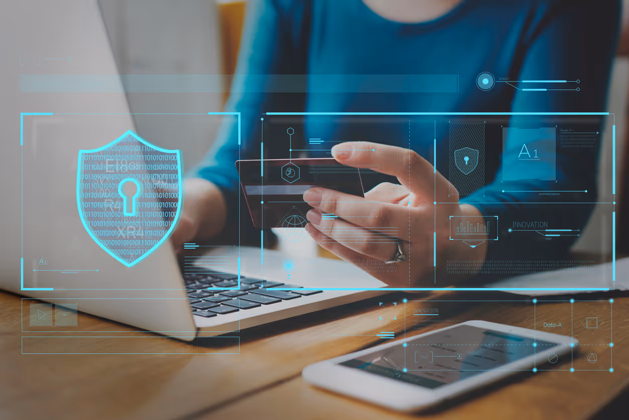 Person holding credit card in front of a laptop with digital security shield and technology icons overlay.