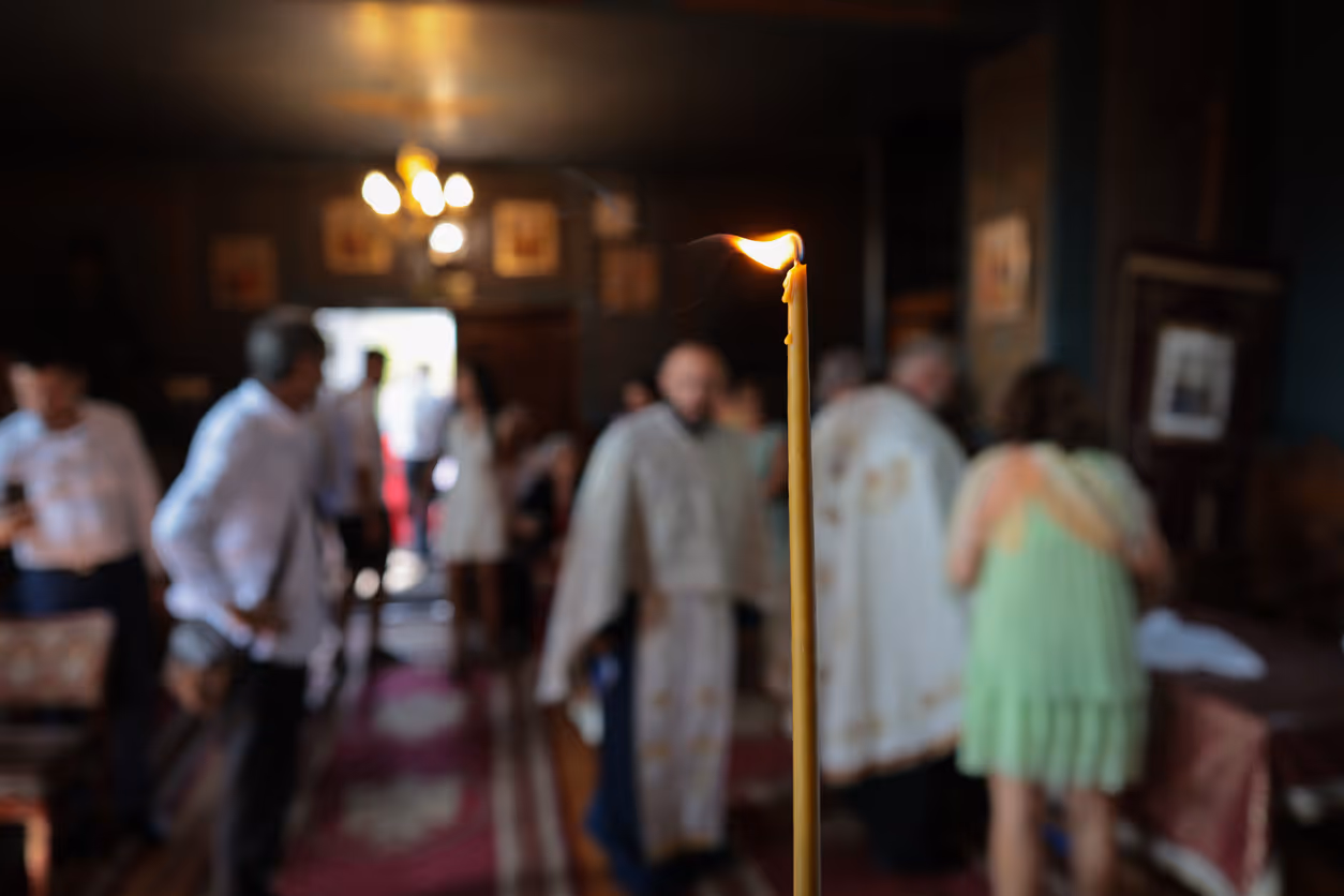 Clergyman in black robe with white and gold embroidered stole holding a smartphone over an open religious book.