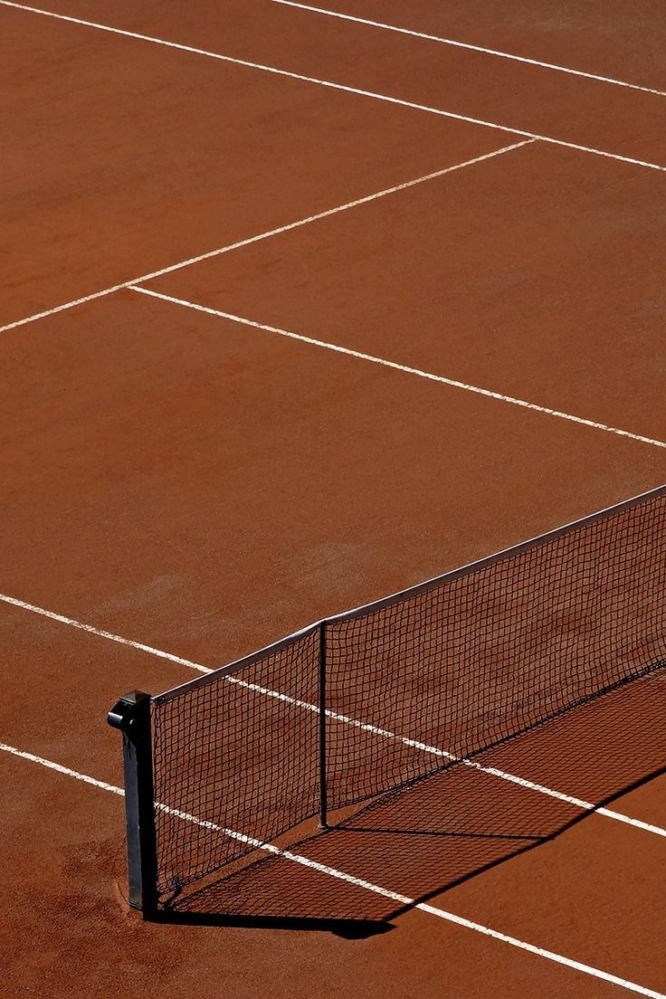 Close-up of a clay tennis court with a black net casting a shadow on the surface.