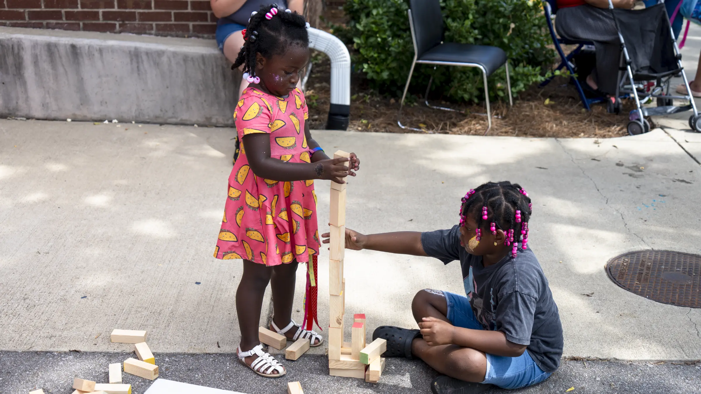 Two young community children play with blocks on the side walk outside The Store at a previous The School Store event