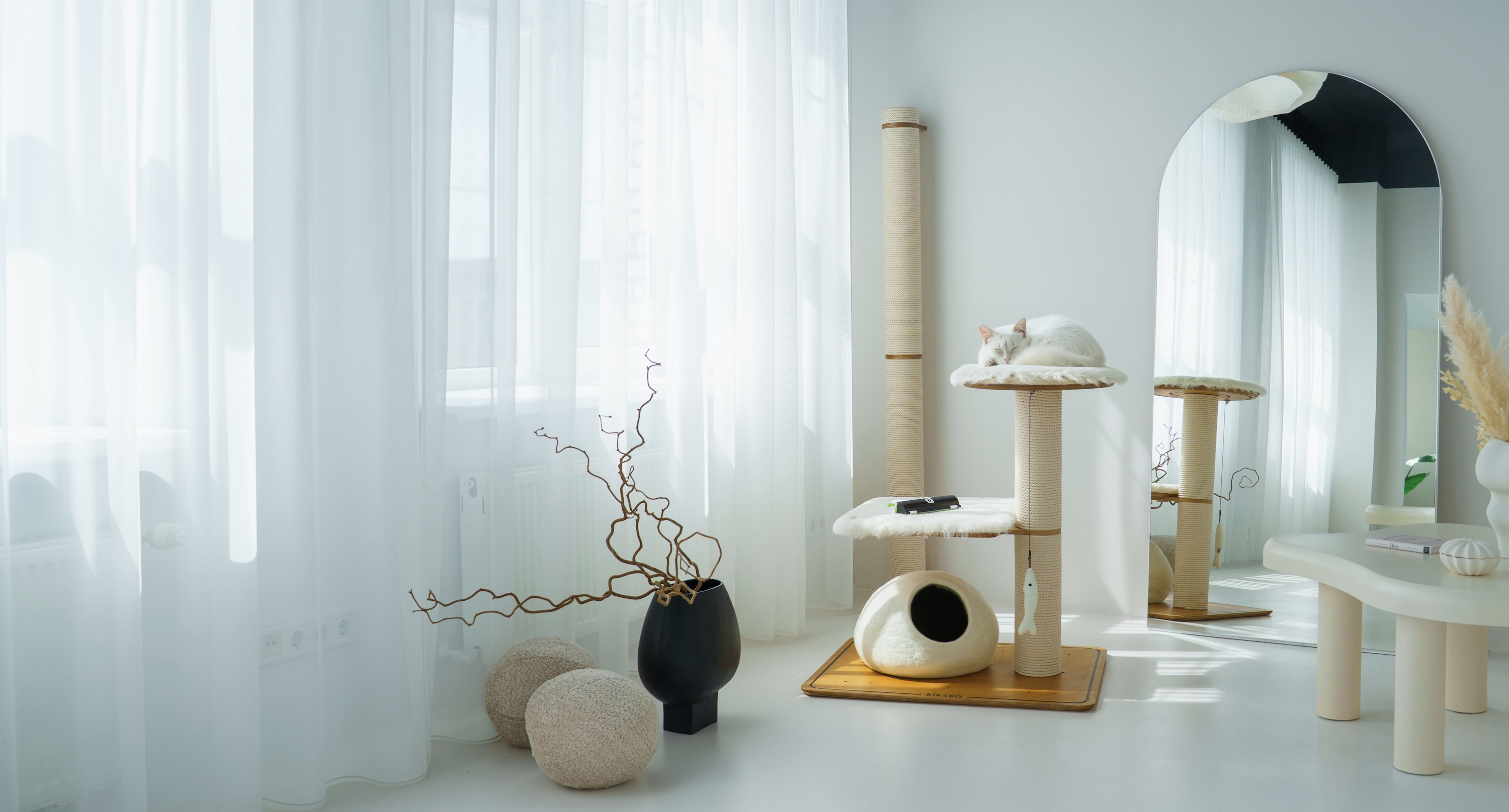 A Kikska cat tree with cotton rope posts, faux fur platforms and a felted wool cave in a bright white room