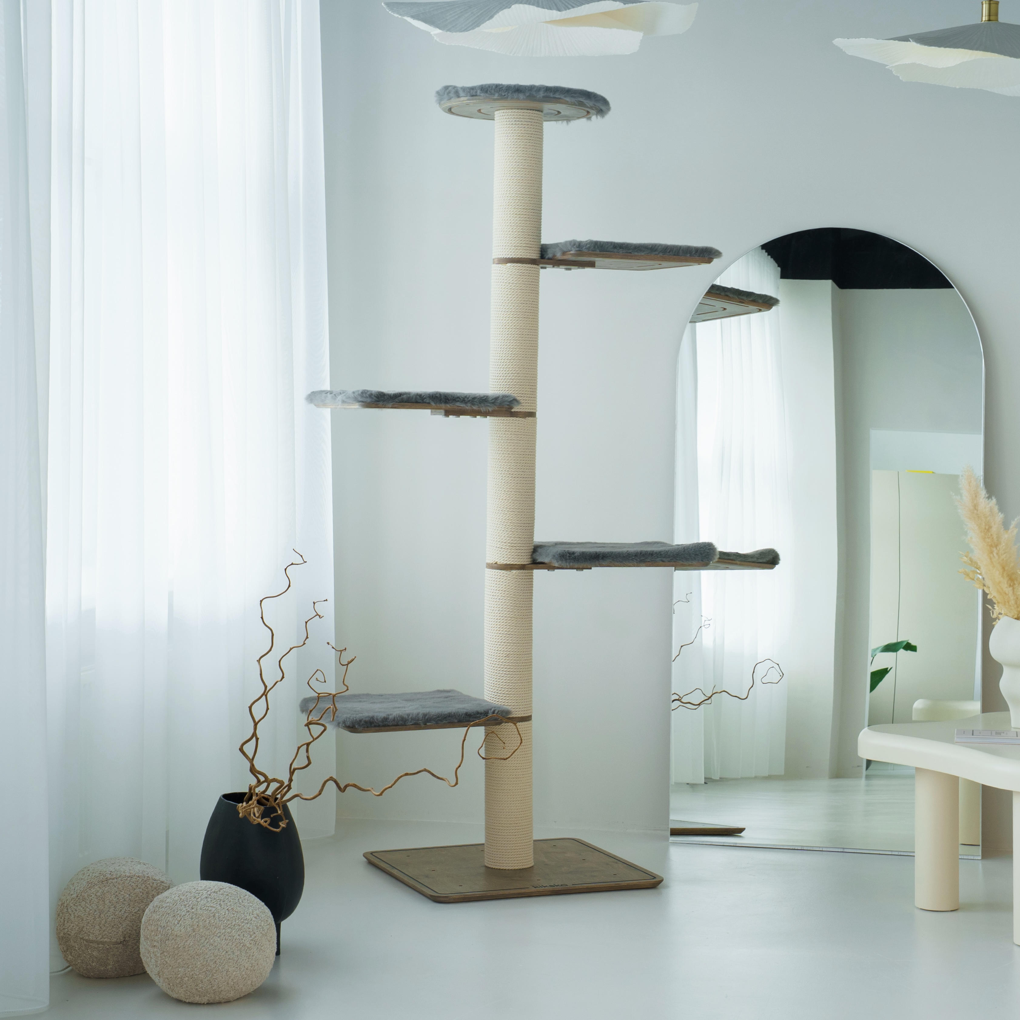Tall Kikska cat tree with several platforms and a wool cave in a bright room