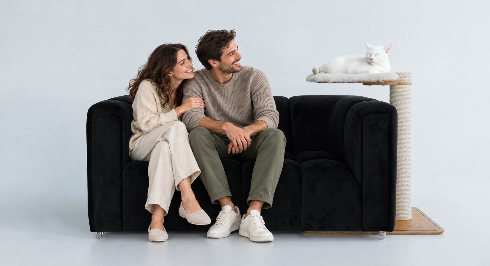 Couple on a black sofa with a white cat resting on a Kikska side perch tucked beside it