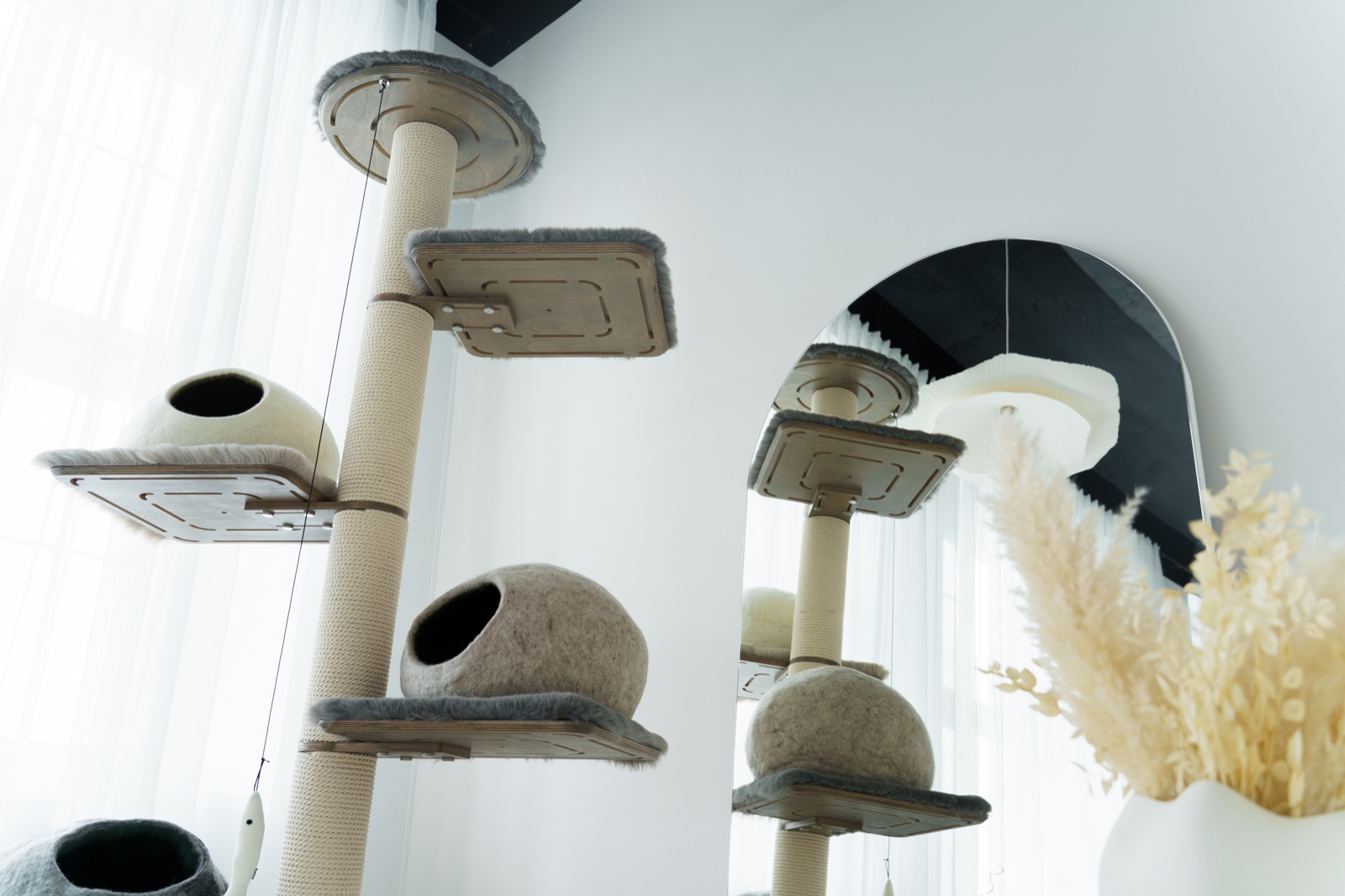 Tall Kikska cat tree with grey faux-fur platforms and wool caves, seen from below, beside an arched mirror
