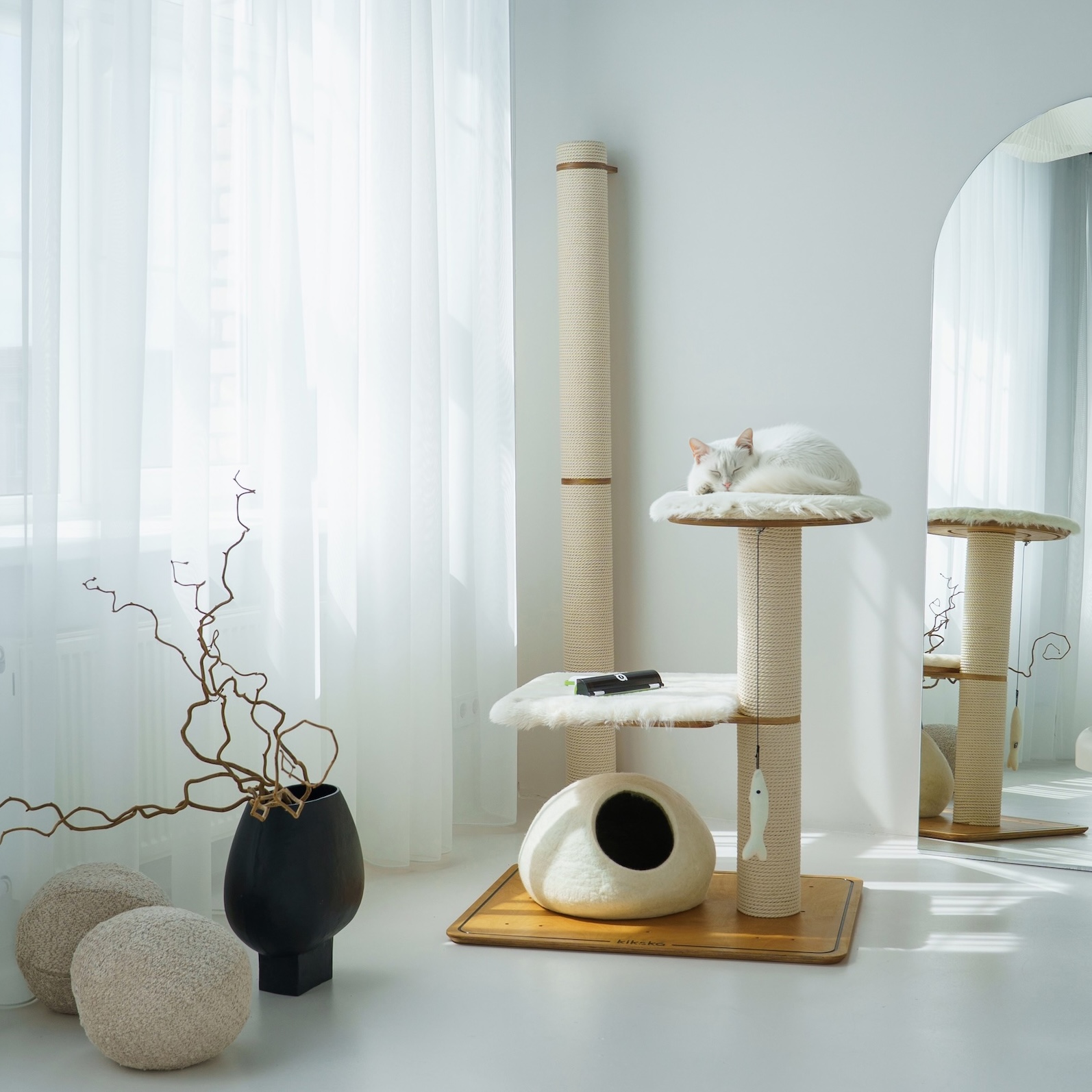 White cat asleep on a standing Kikska cat tree with a wool cave, beside a tall rope post