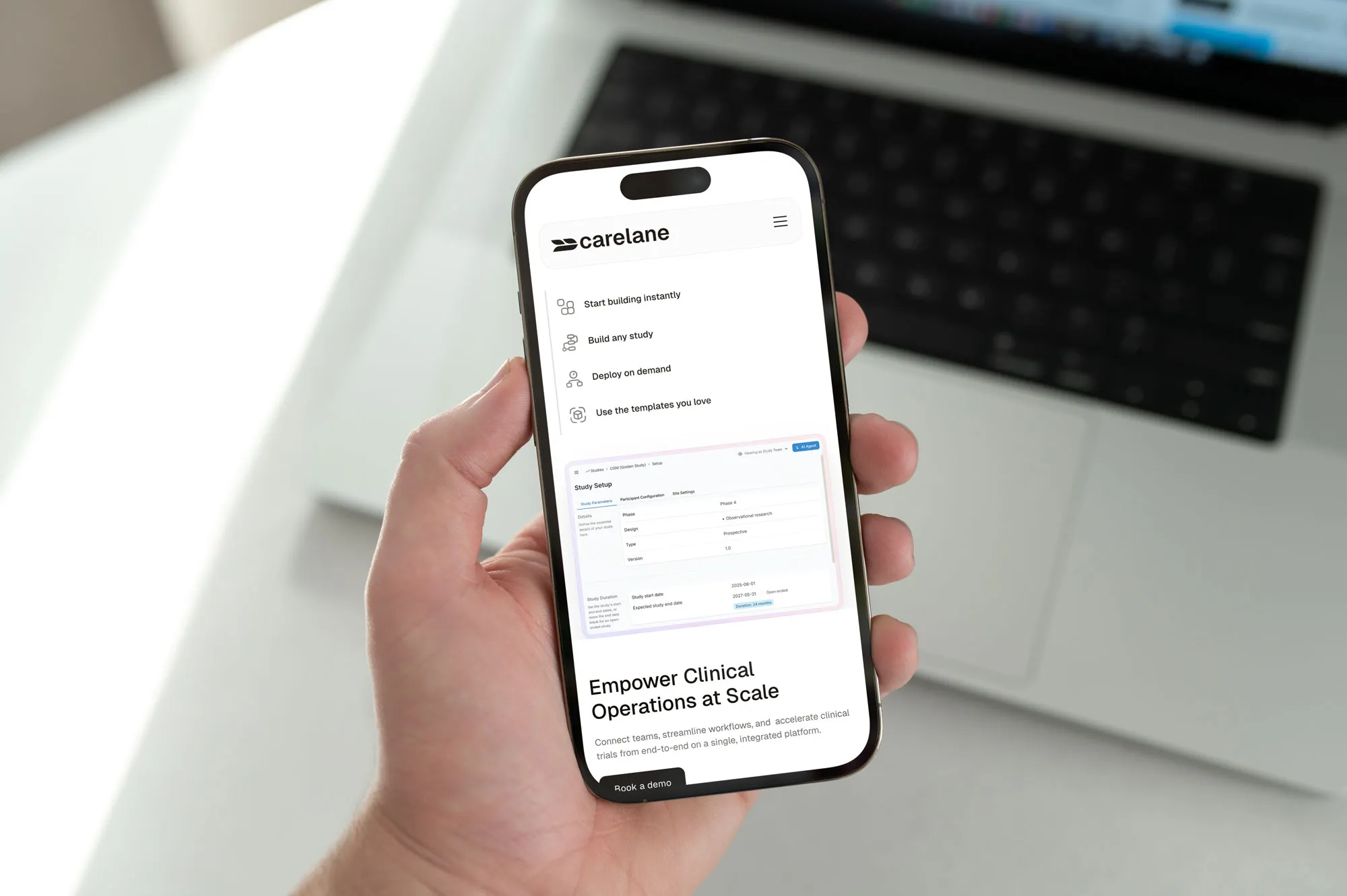 Hand hält ein Smartphone mit geöffneter Webseite vor einem Laptop