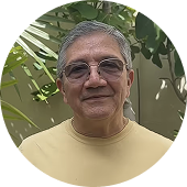 Hombre mayor con gafas y camiseta amarilla sonriente delante de plantas verdes.