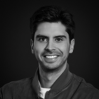 Retrato en blanco y negro de un hombre joven sonriendo con una camisa oscura y fondo oscuro.