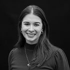 Retrato en blanco y negro de una mujer joven con cabello largo y liso, sonriendo, usando pendientes y collar sobre fondo oscuro.