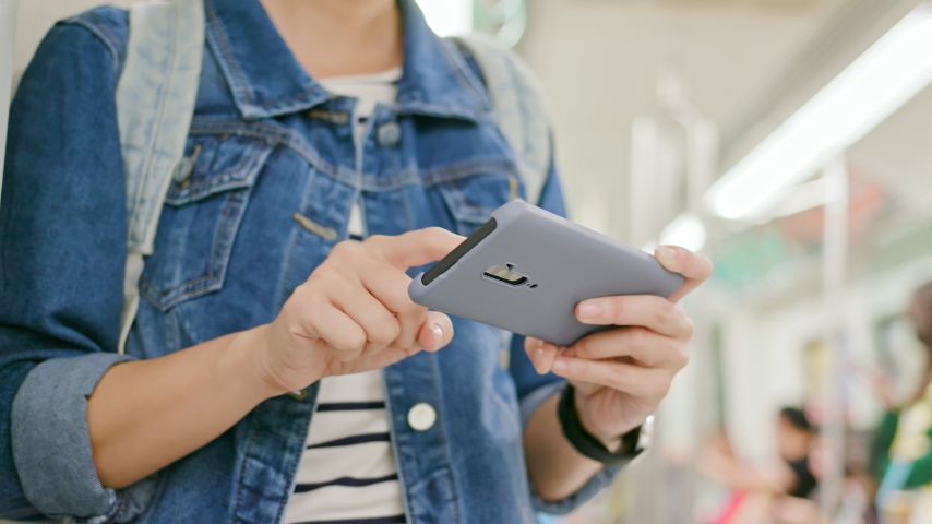 Persona usando un teléfono móvil para realizar una operación bancaria en línea, dentro del metro. Ilustra el artículo Cómo transferir dinero de una cuenta a otra desde el celular.