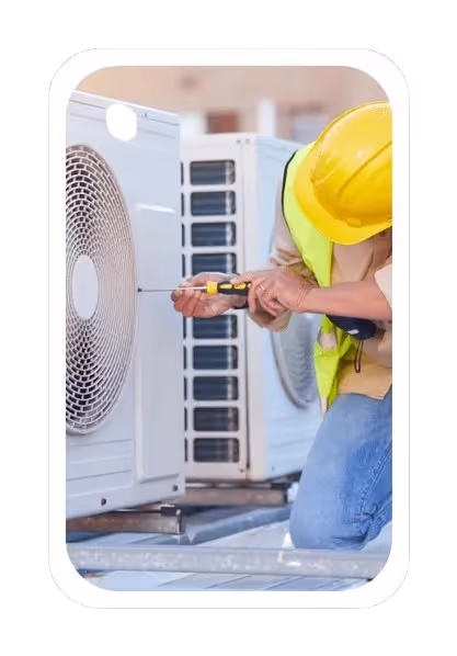  A close-up, portrait-oriented image framed with rounded corners, shows a technician in a yellow hard hat and safety vest working on an outdoor HVAC unit. He is kneeling and using a screwdriver on the side of a white unit with a circular fan grill. Another similar unit is visible in the background.