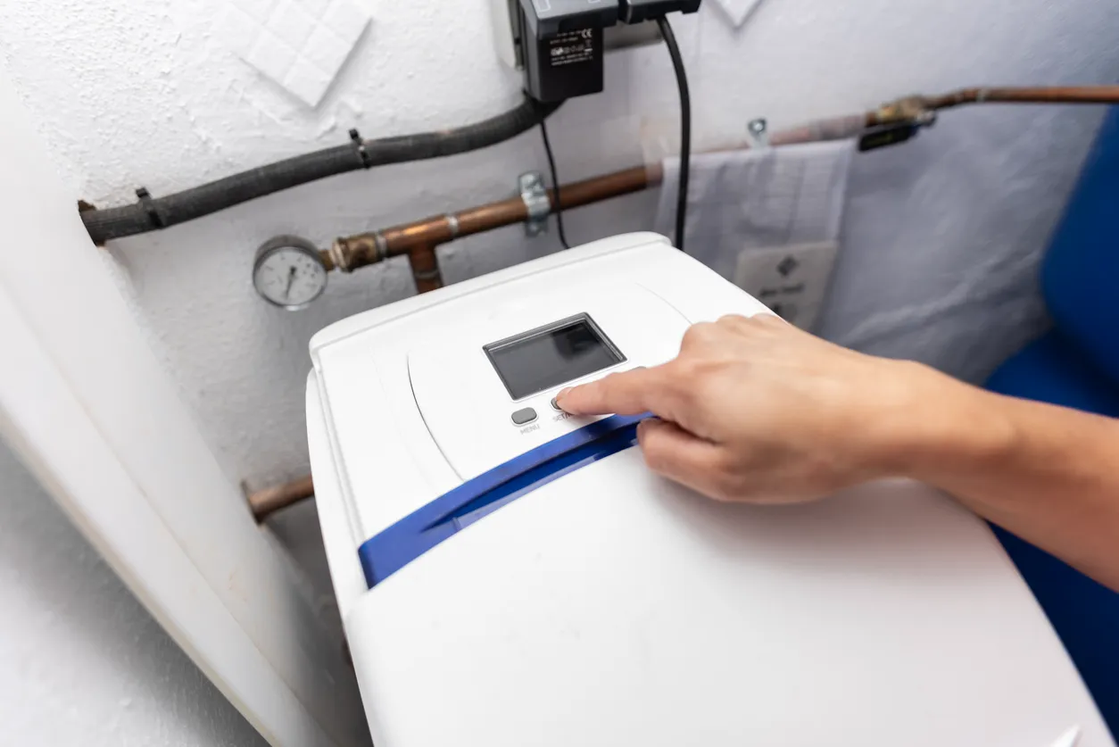 A hand operating the control panel of a white household water softener unit