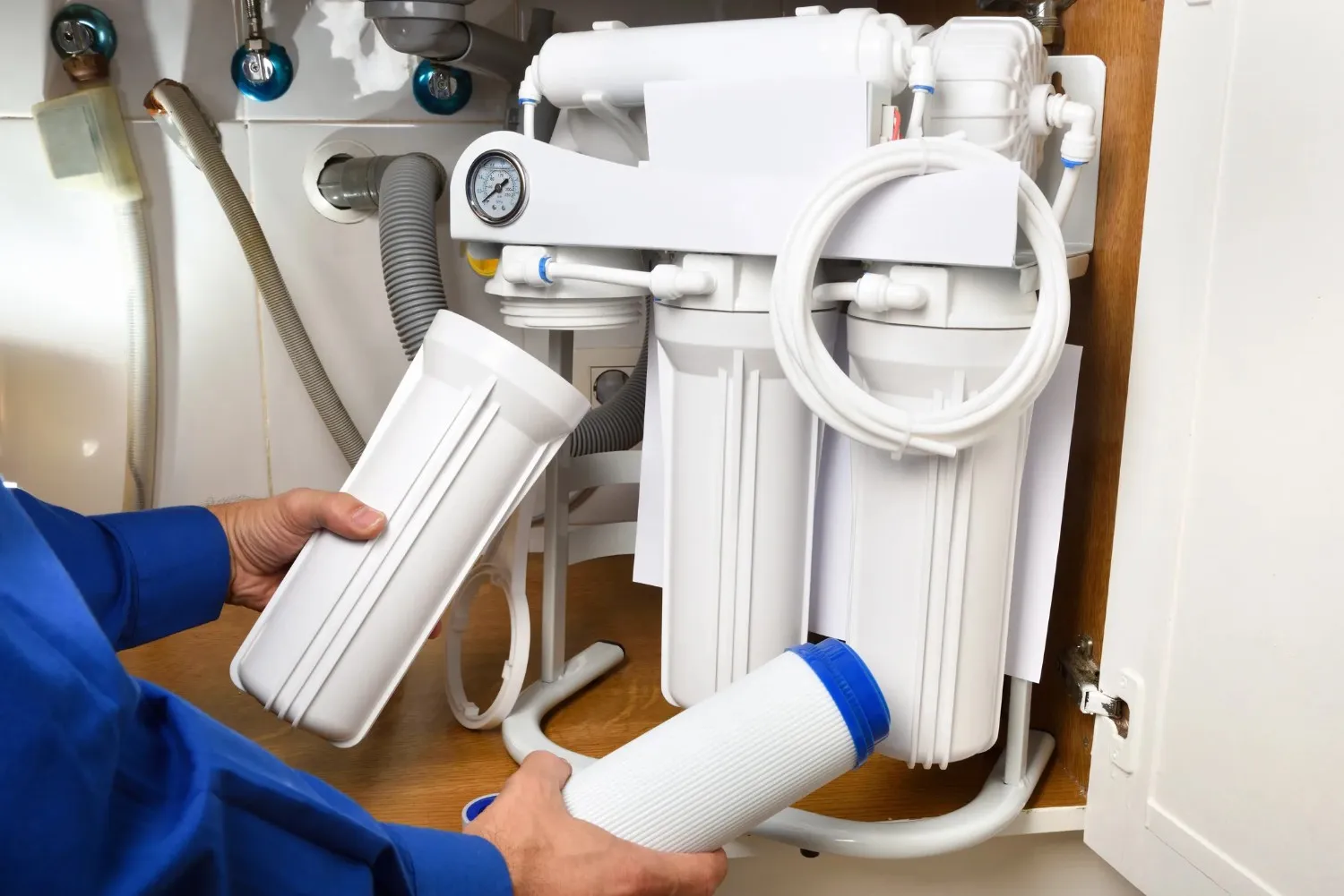 A person's hands holding water filter cartridges, with an under-sink water filtration system in the background