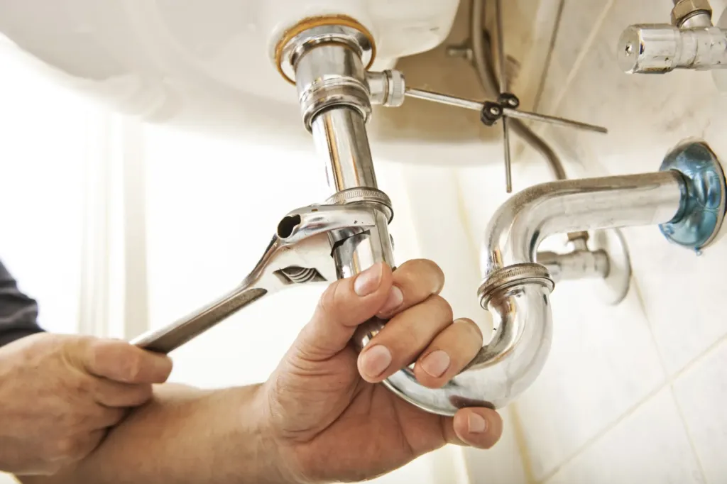 Hands tightening plumbing pipes with wrench.
