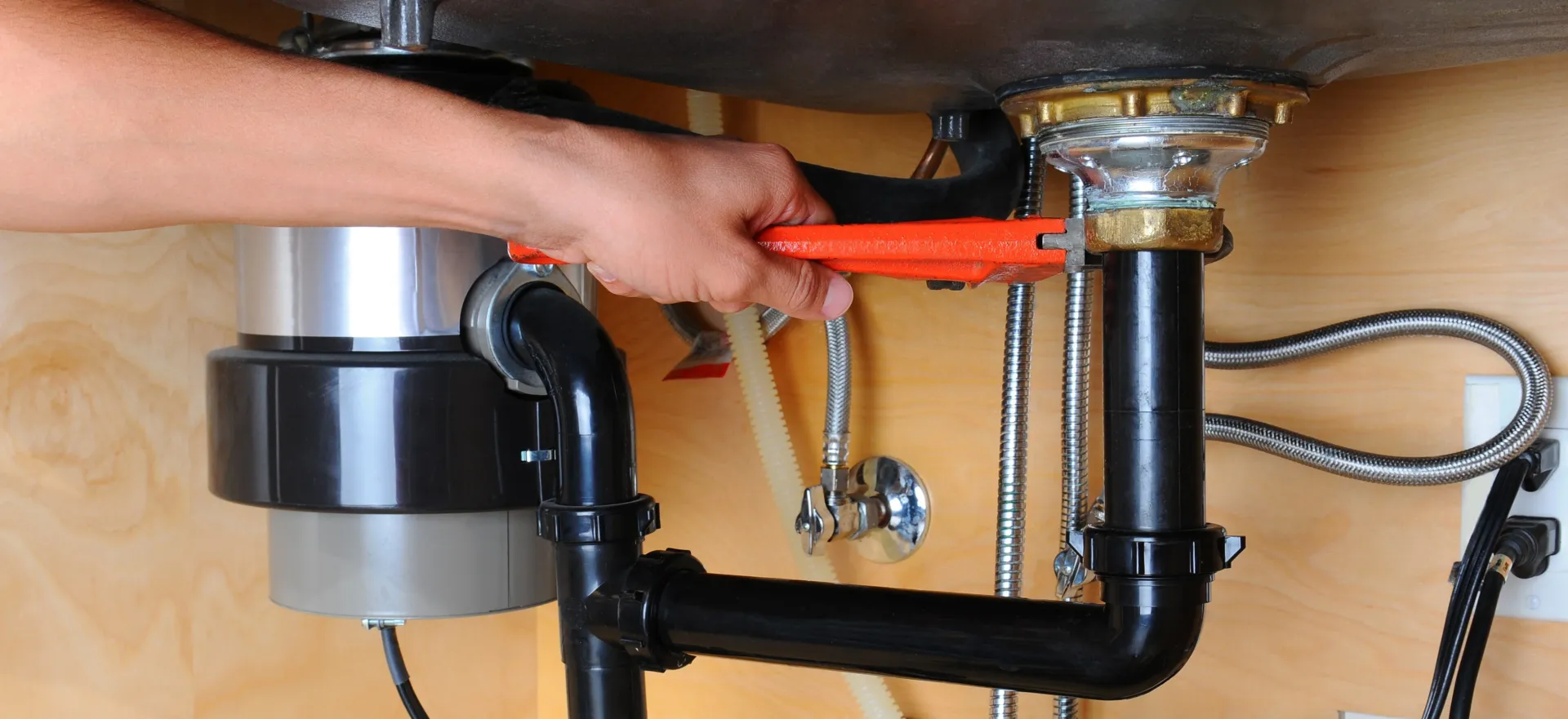 A close shot of a persons hand repairing an under sink garbage disposal system