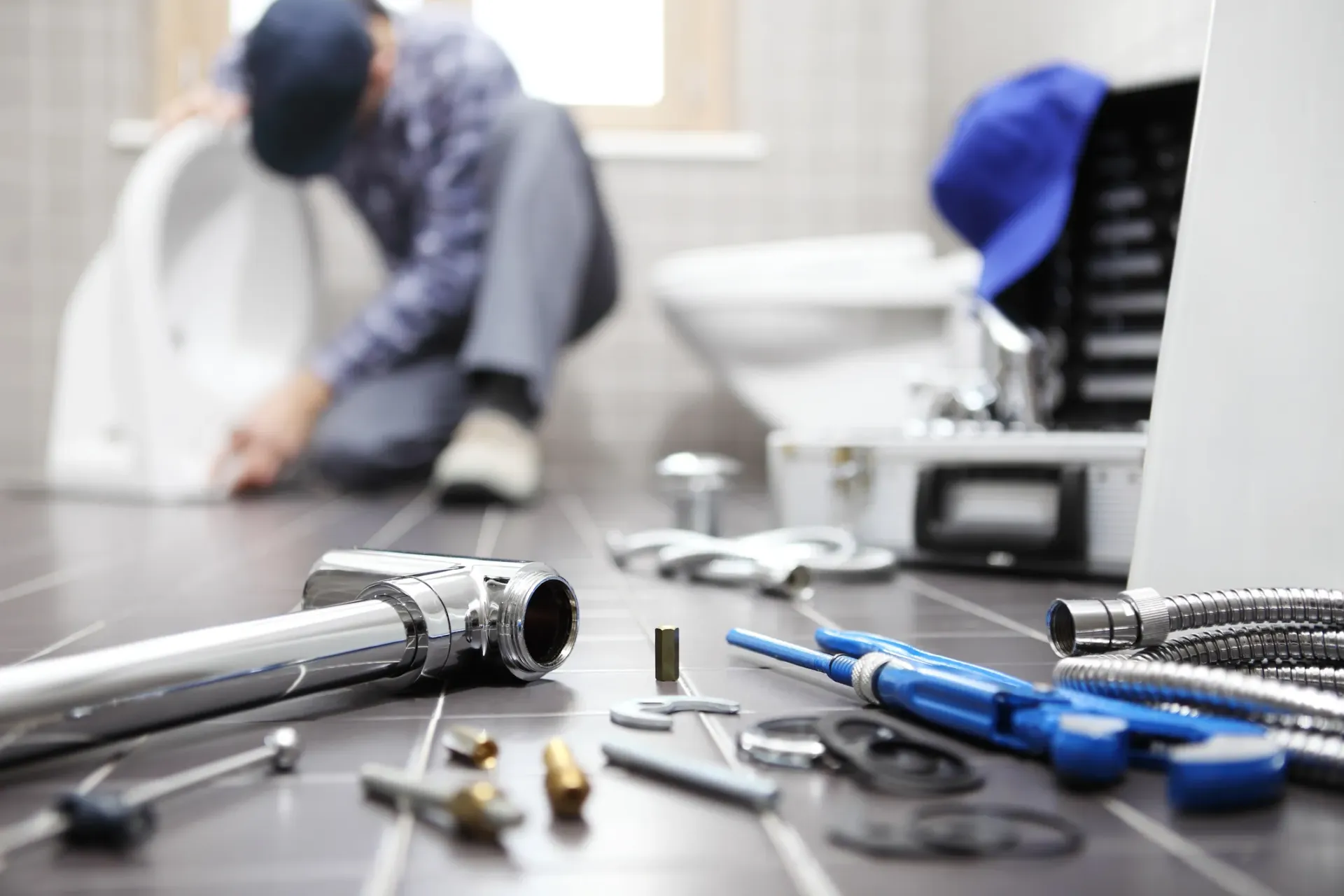 A close up shot of tools and equipments for toilet repair with a plumber working in the background