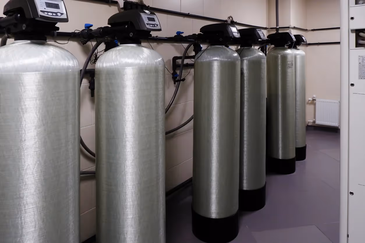 A row of large, cylindrical water softening tanks in an industrial or commercial setting
